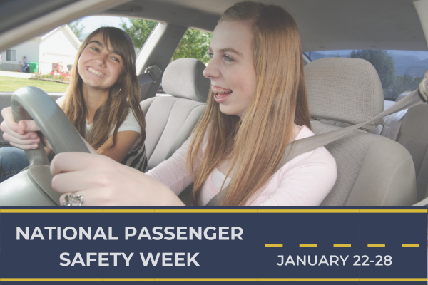 Two individuals are seated in the front seats of a car. The person on the left is in the driver's seat, holding the steering wheel, while the person on the right is in the passenger seat, wearing a seatbelt. The image is overlaid with a banner at the bottom that reads 'NATIONAL PASSENGER SAFETY WEEK' on the left and 'JANUARY 22-28' on the right. The background shows a suburban neighborhood with houses and greenery.